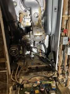 Inside an old boiler: dirty, corroded burner area, pump and exposed circuit board